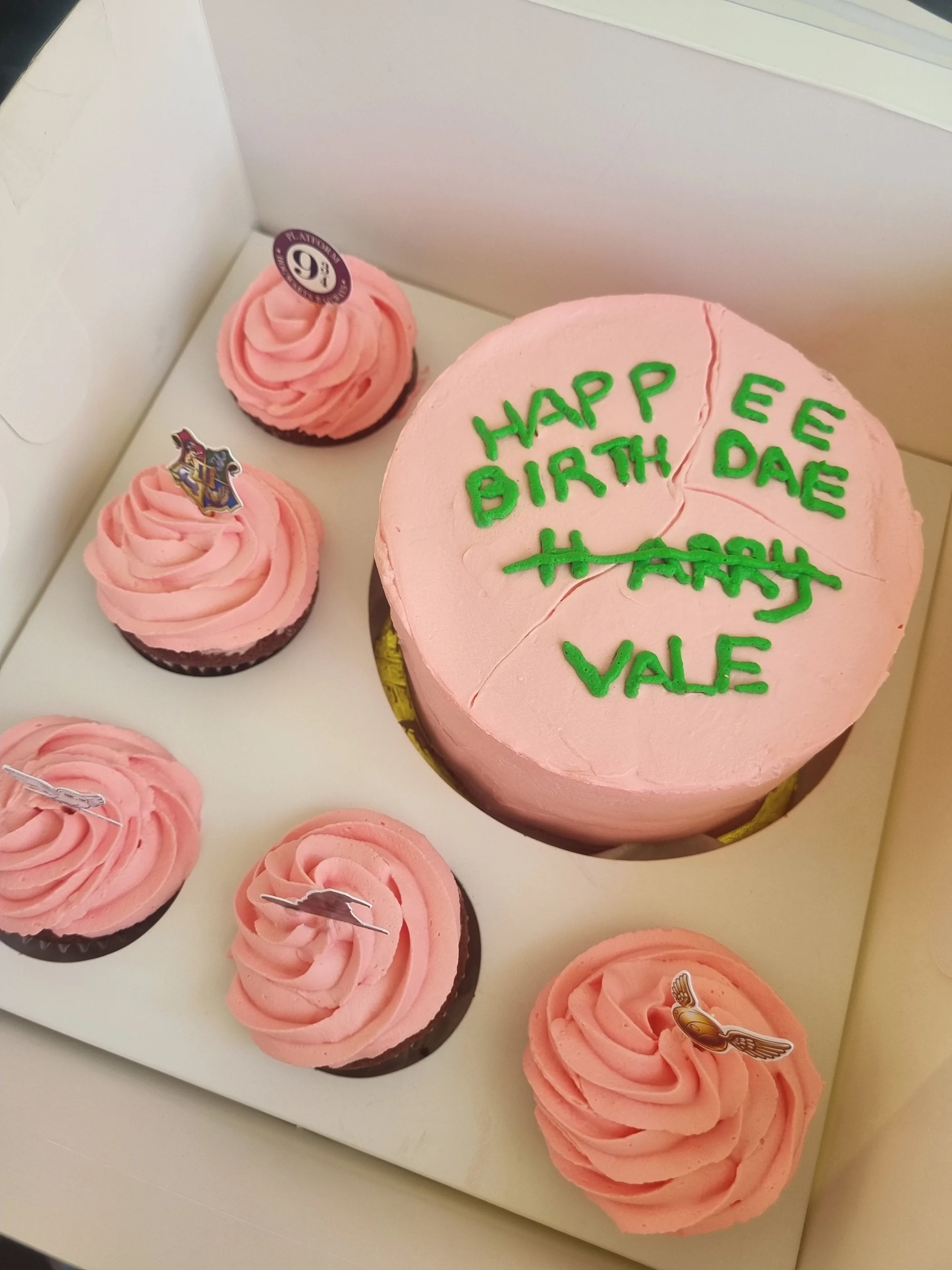Torta rosa con mensaje verde de cumpleaños para Vale y cinco cupcakes con crema rosa sobre una base blanca.