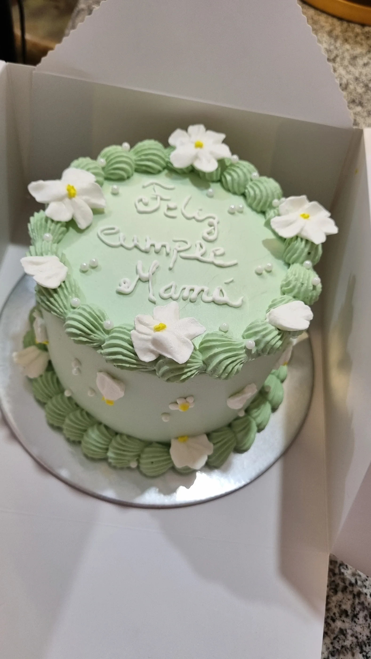 Torta verde pastel con flores blancas de centro amarillo y mensaje de cumpleaños.