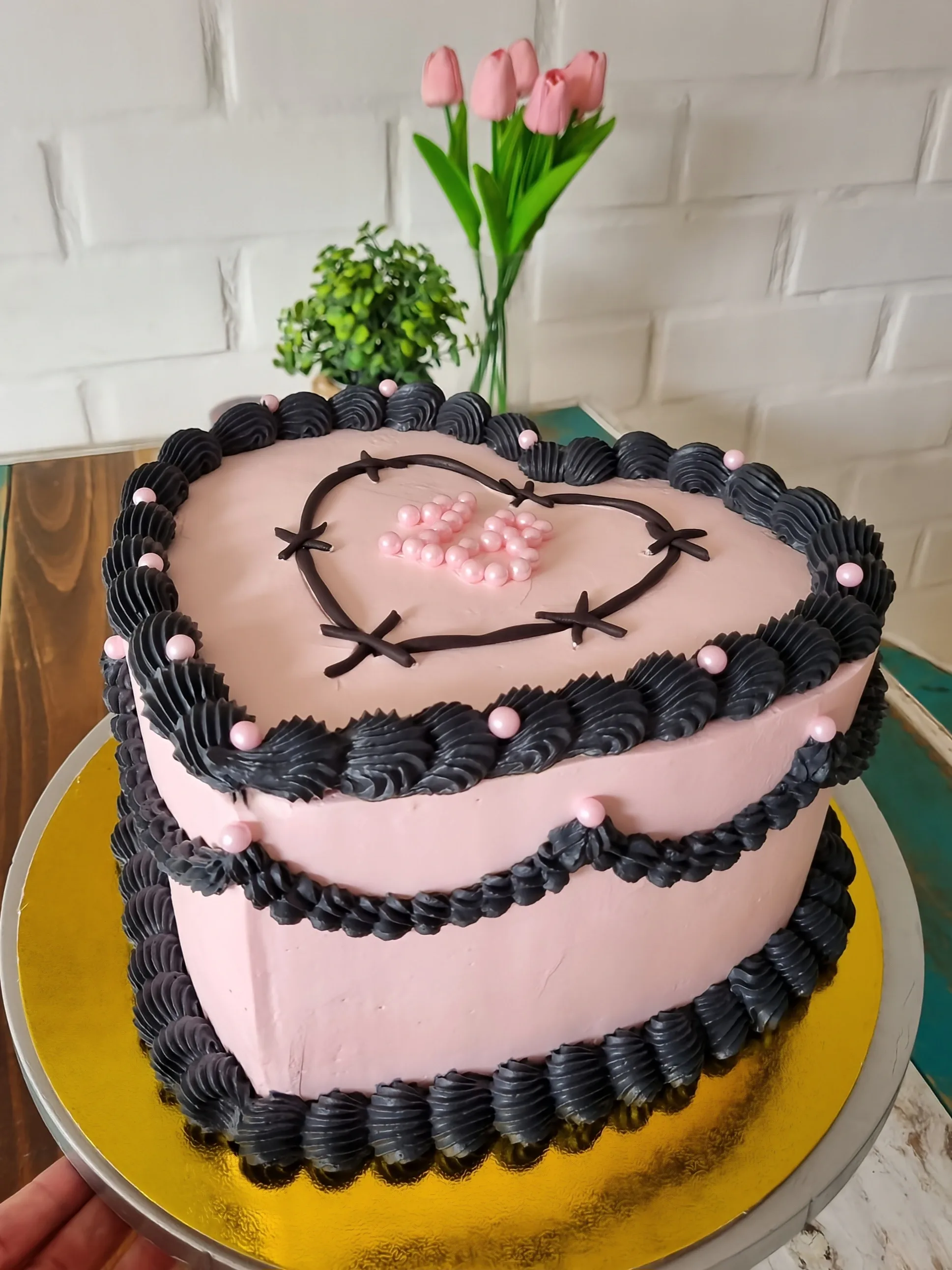 Torta corazón rosa con volantes negros, perlas rosadas y corazón negro dibujado en la superficie.