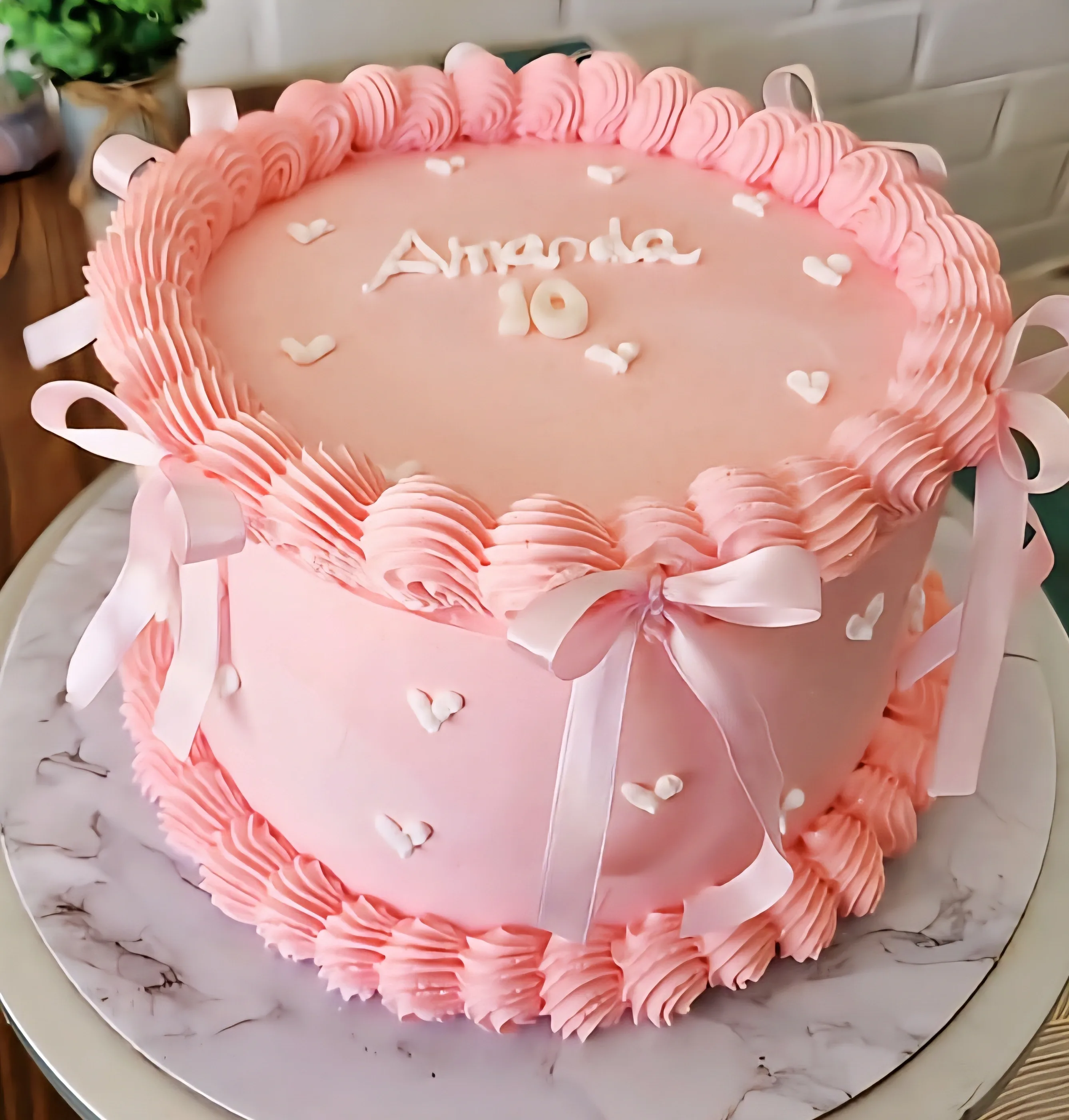 Torta rosa con volantes de crema, corazones blancos, lazos de satén y nombre Amanda.