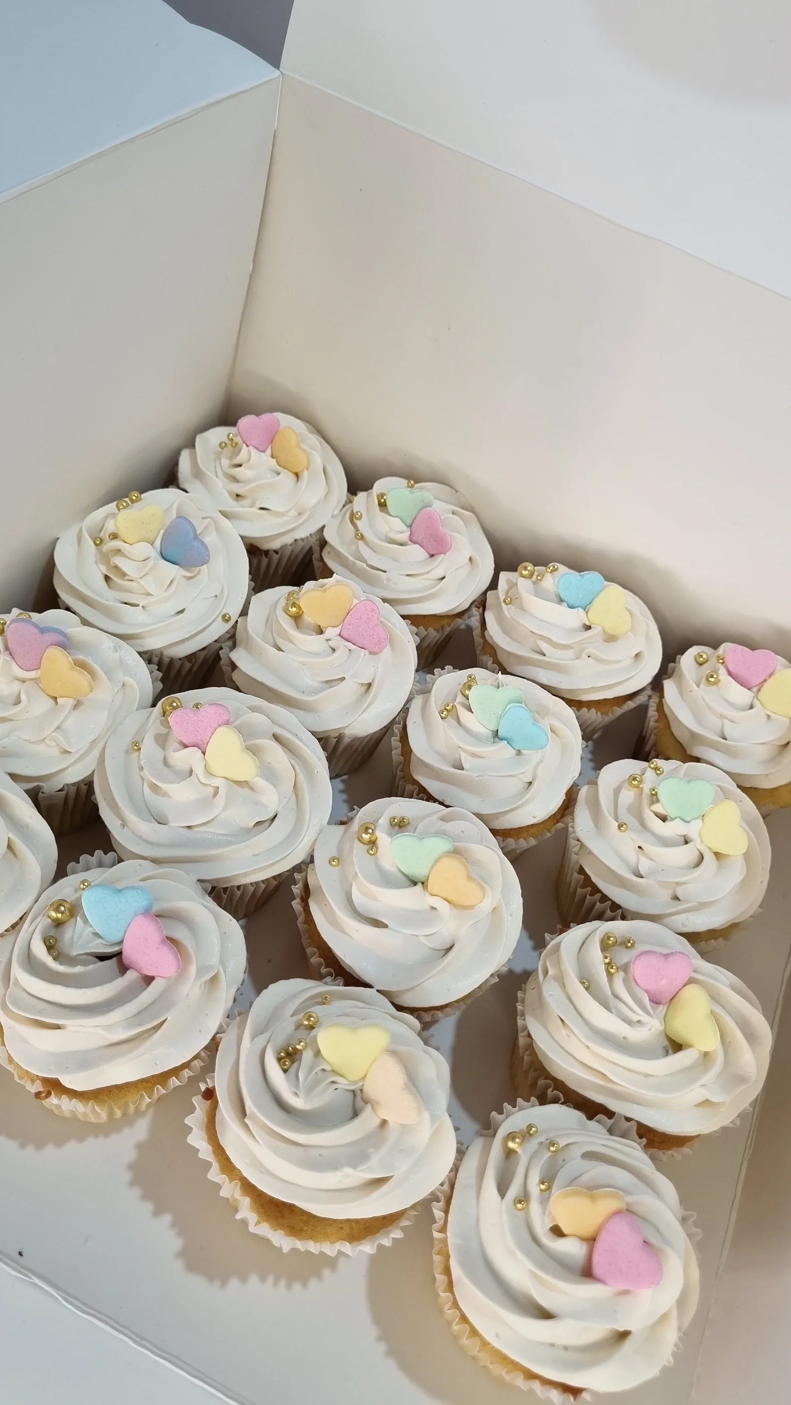 Conjunto de cupcakes con espirales de crema blanca y pequeños detalles en tonos pastel sobre una base blanca.