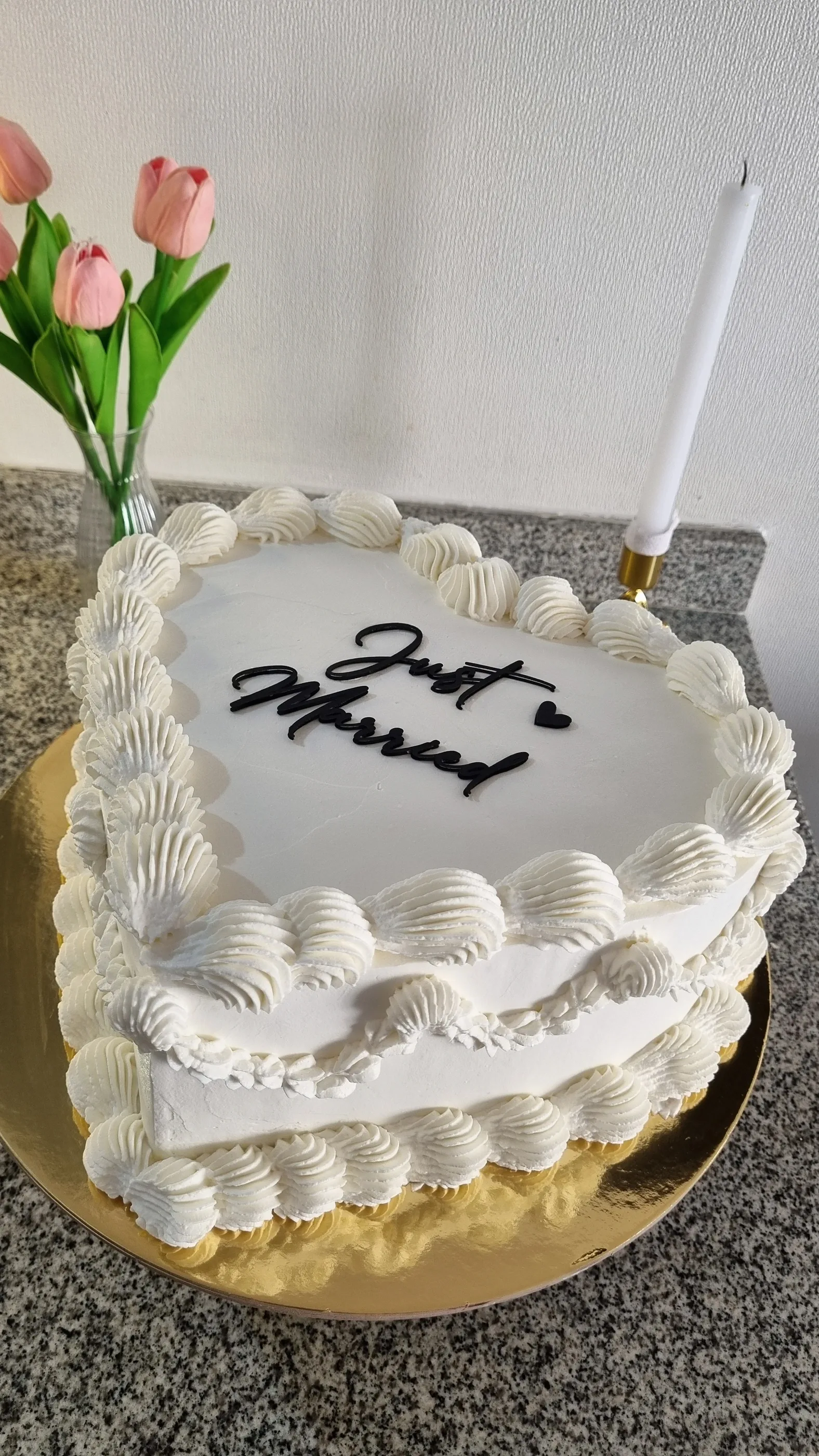 Torta blanca con bordes de crema, inscripción negra Just Married y una vela blanca alta.