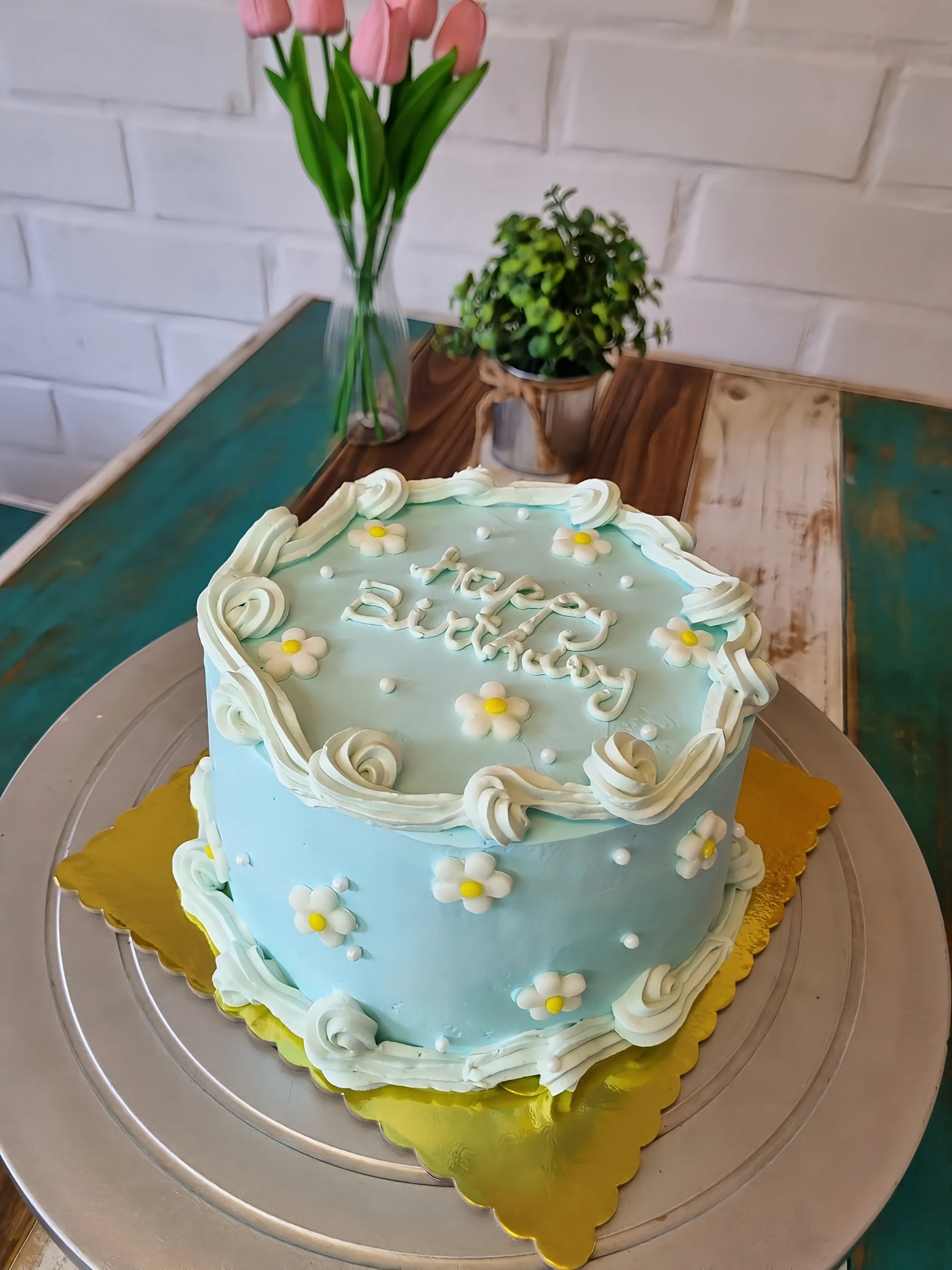 Torta celeste con margaritas blancas, perlas, bordes de crema y mensaje de cumpleaños.