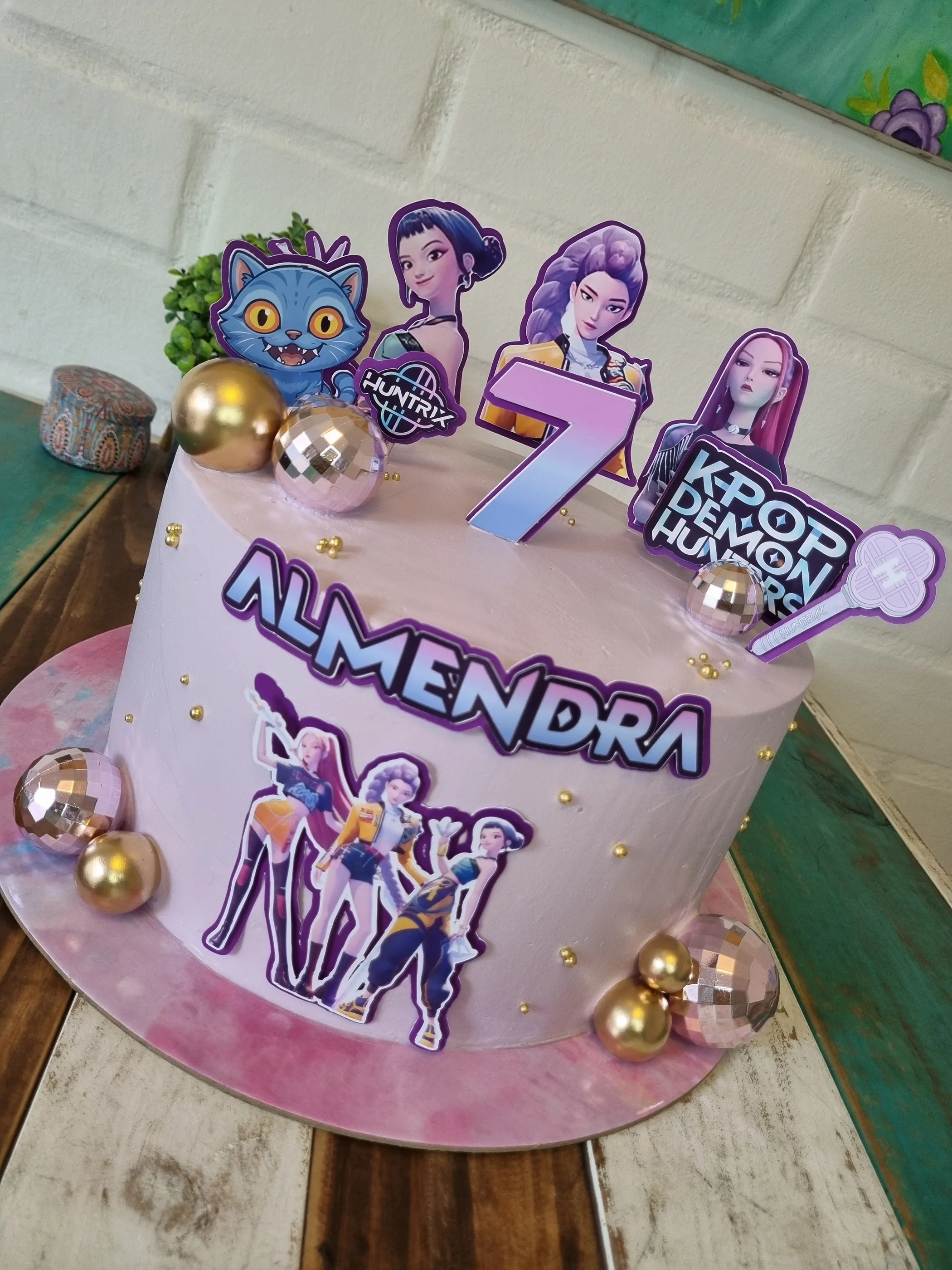 Torta lila con personajes de K-pop, esferas metálicas, nombre Almendra y número 7.