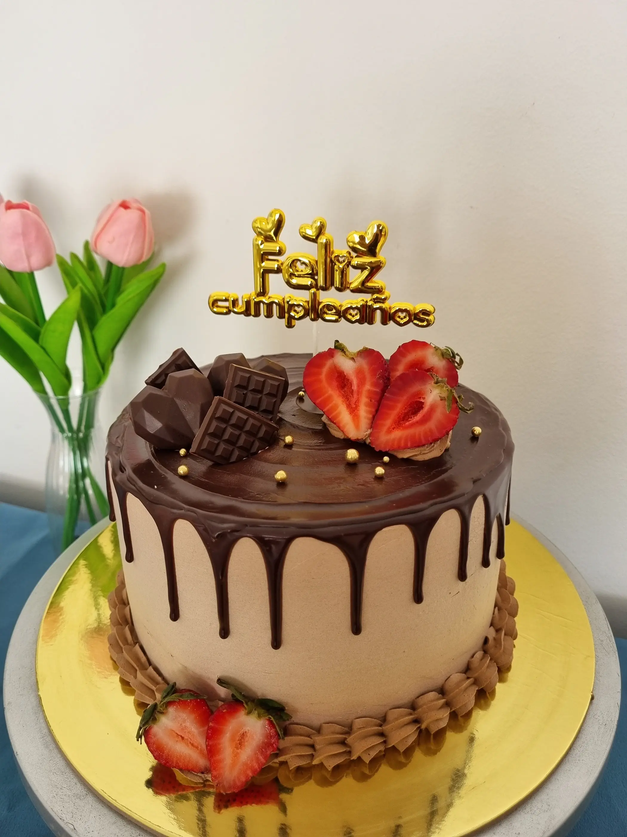 Torta con cobertura de chocolate, goteado, trozos de chocolate, frutillas y letrero Feliz cumpleaños.