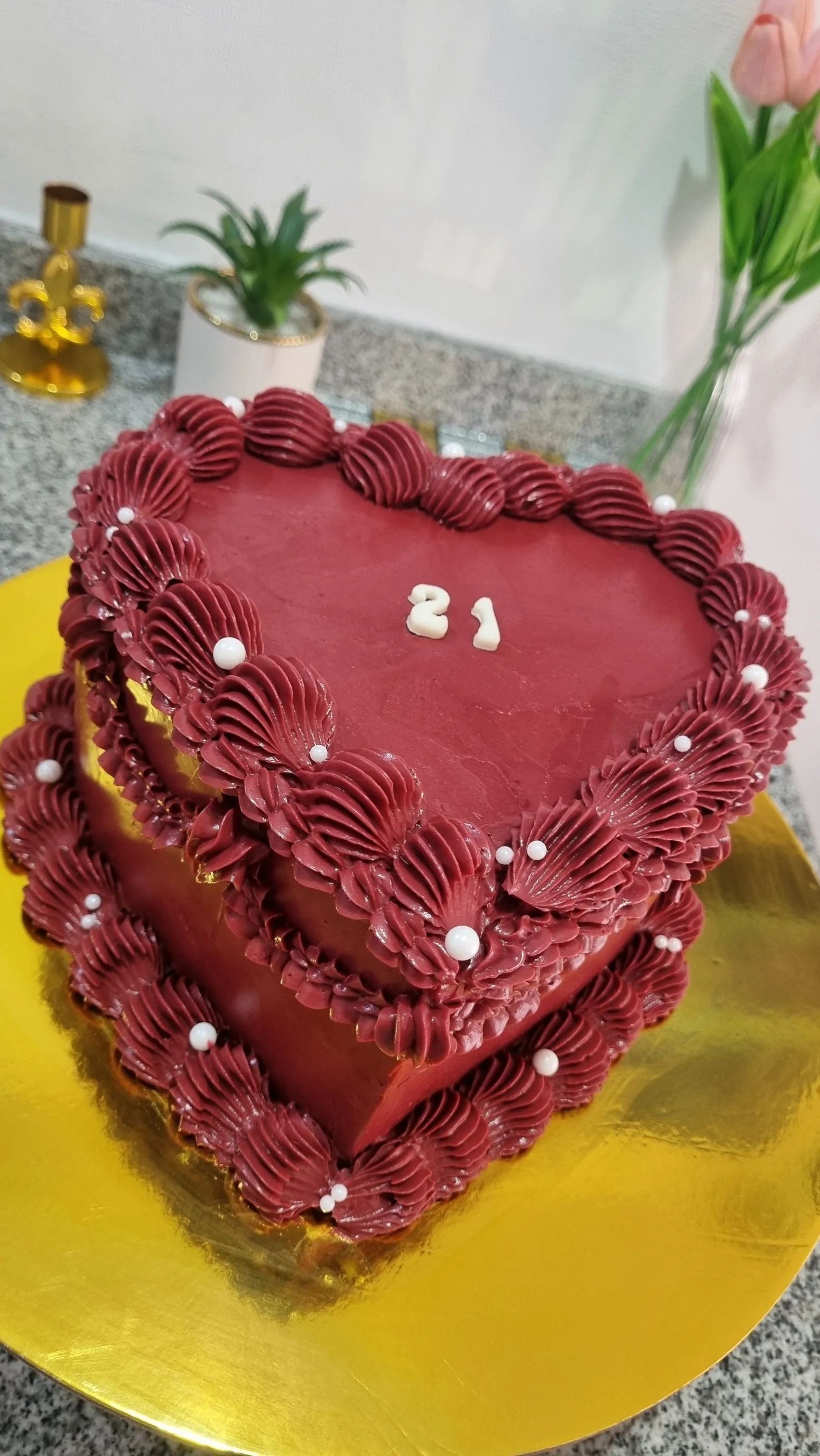 Vista elevada de torta corazón burdeos con volantes de crema, perlas blancas y número 21.