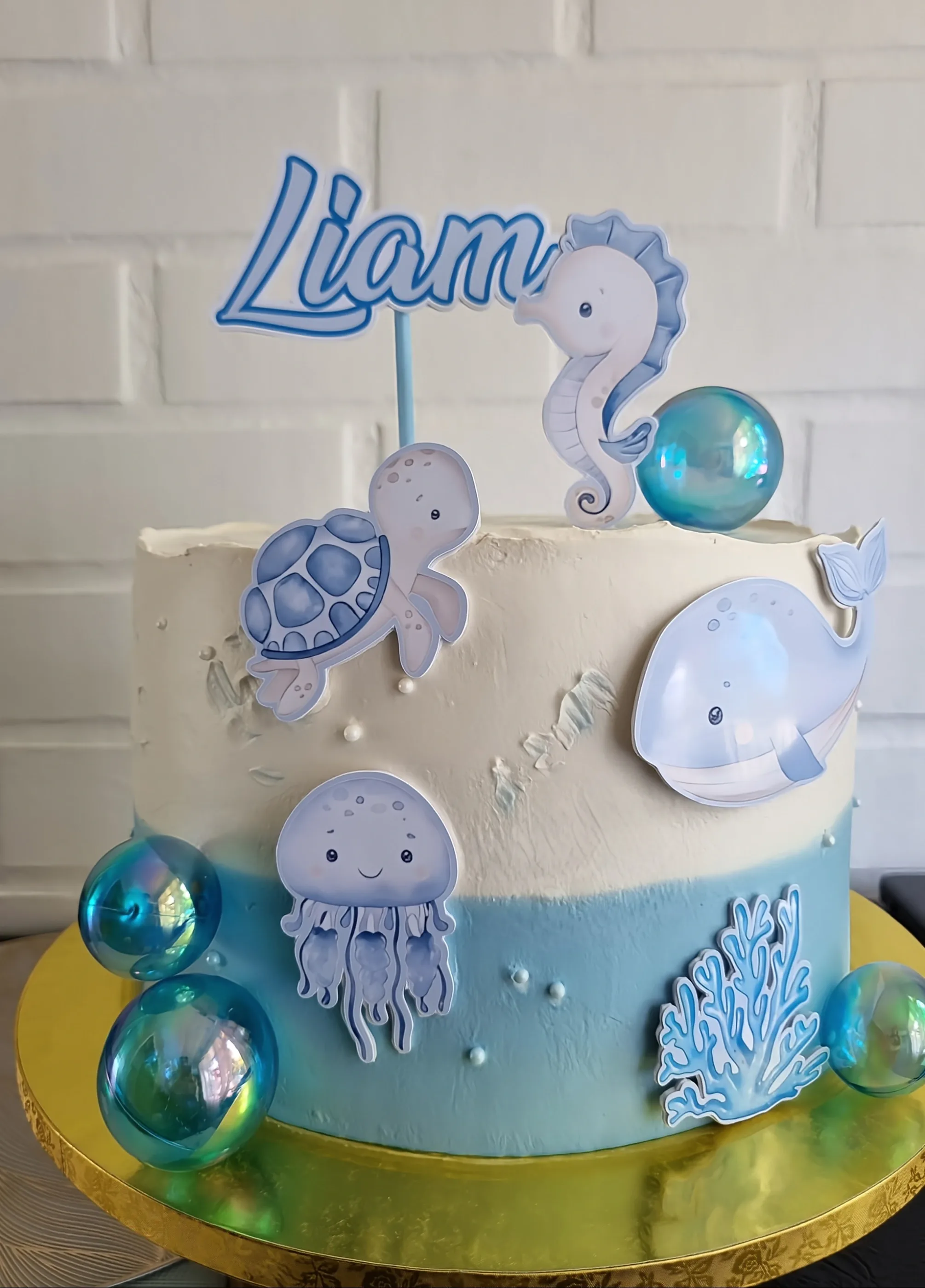 Torta blanca y celeste con nombre Liam, caballito de mar, tortuga, ballena, medusas y esferas transparentes.