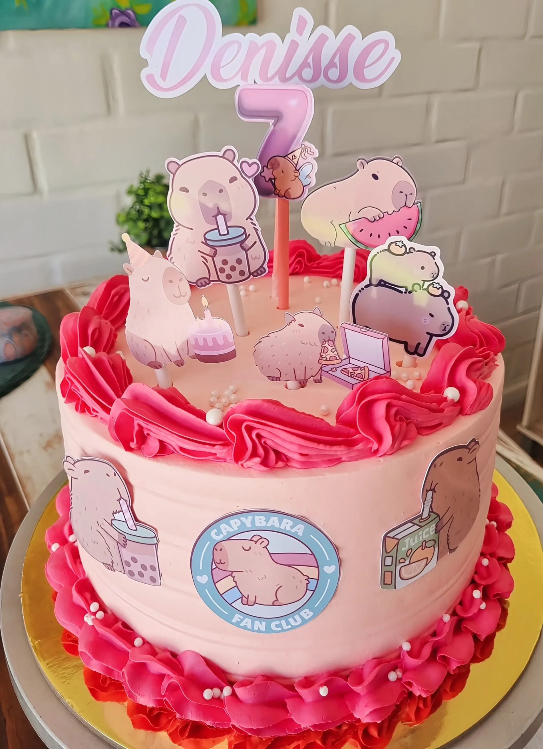 Torta rosa con bordes fucsia, figuras de capibaras, nombre Denise y número 7.