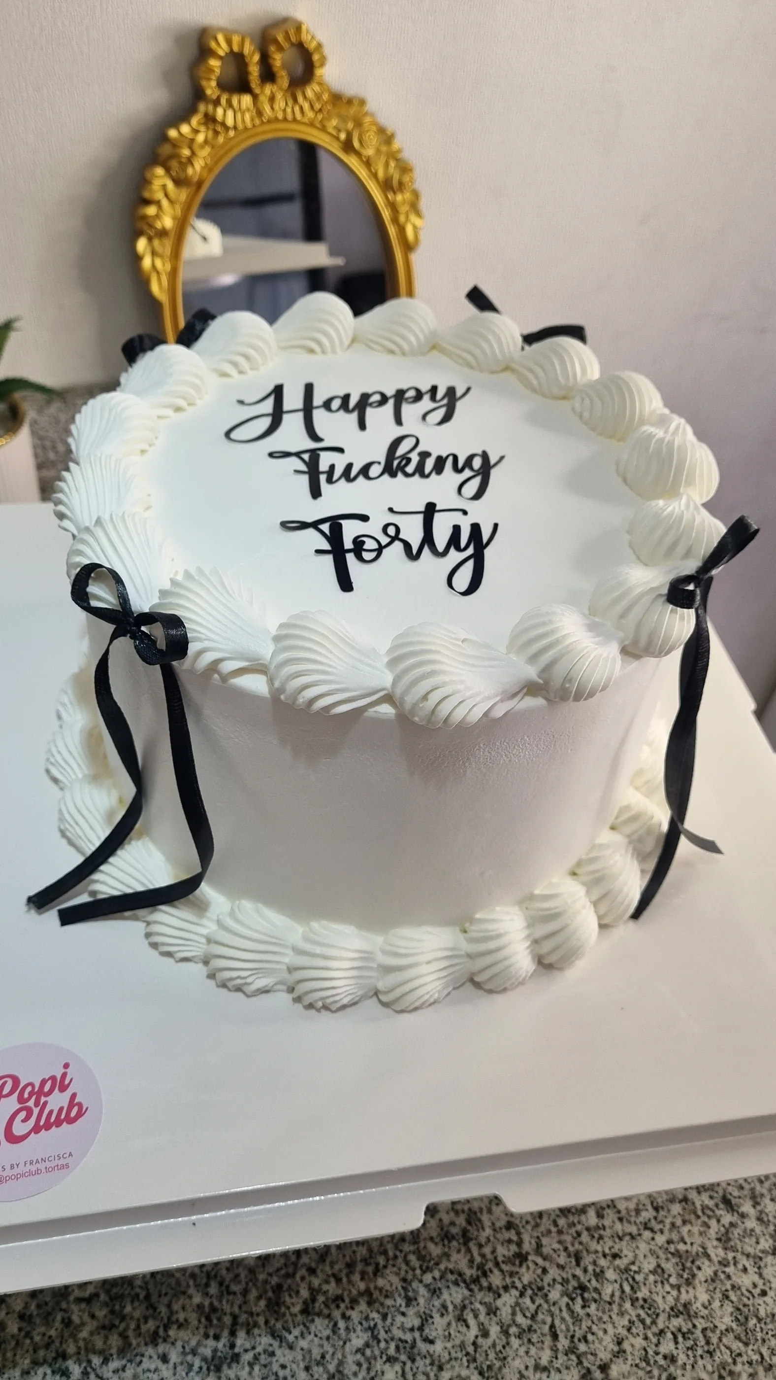 Torta blanca con bordes de crema, lazos negros e inscripción Happy Fucking Forty.