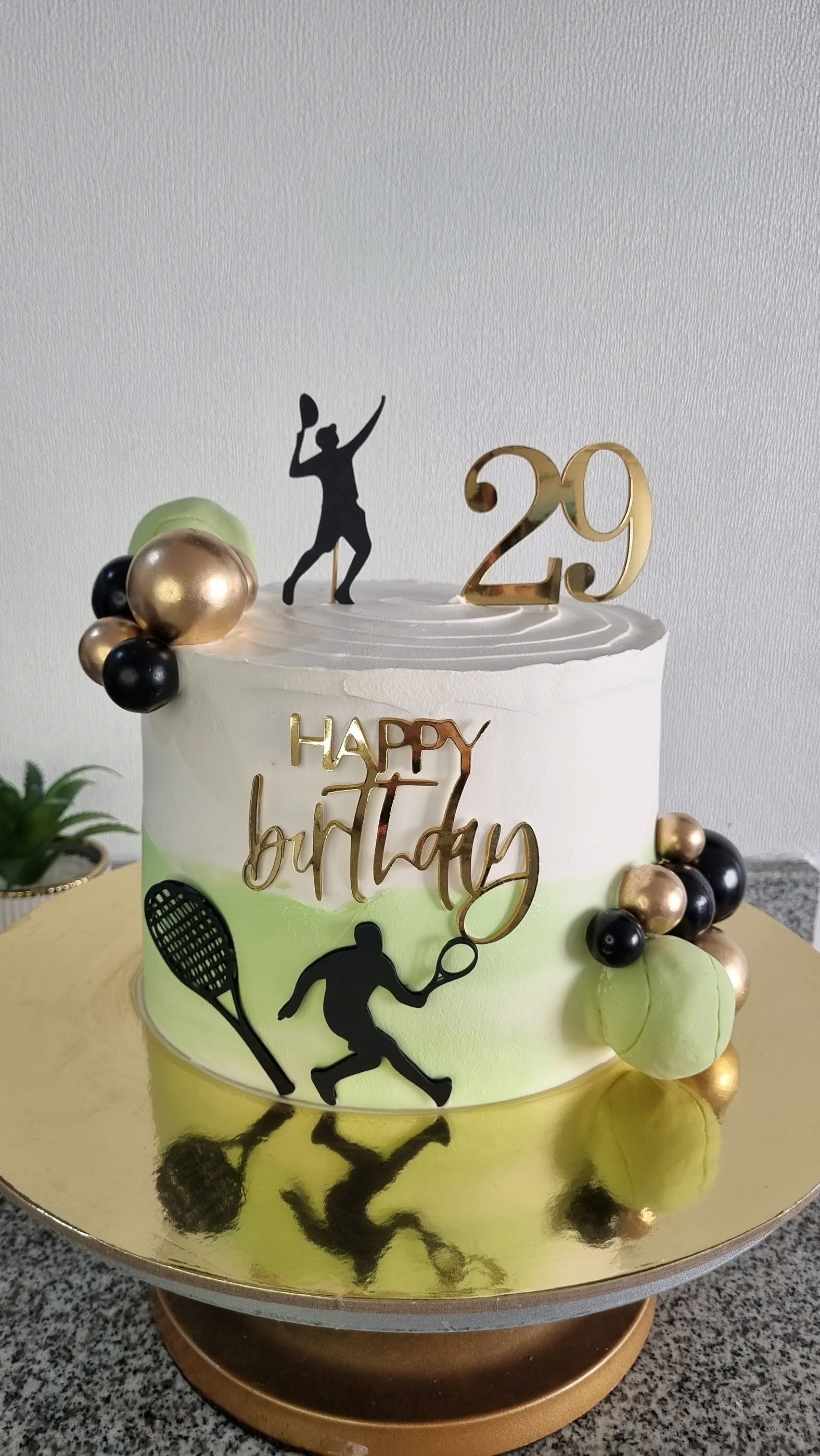 Torta blanca con siluetas de tenistas, raqueta, pelotas verdes, esferas y número 29.