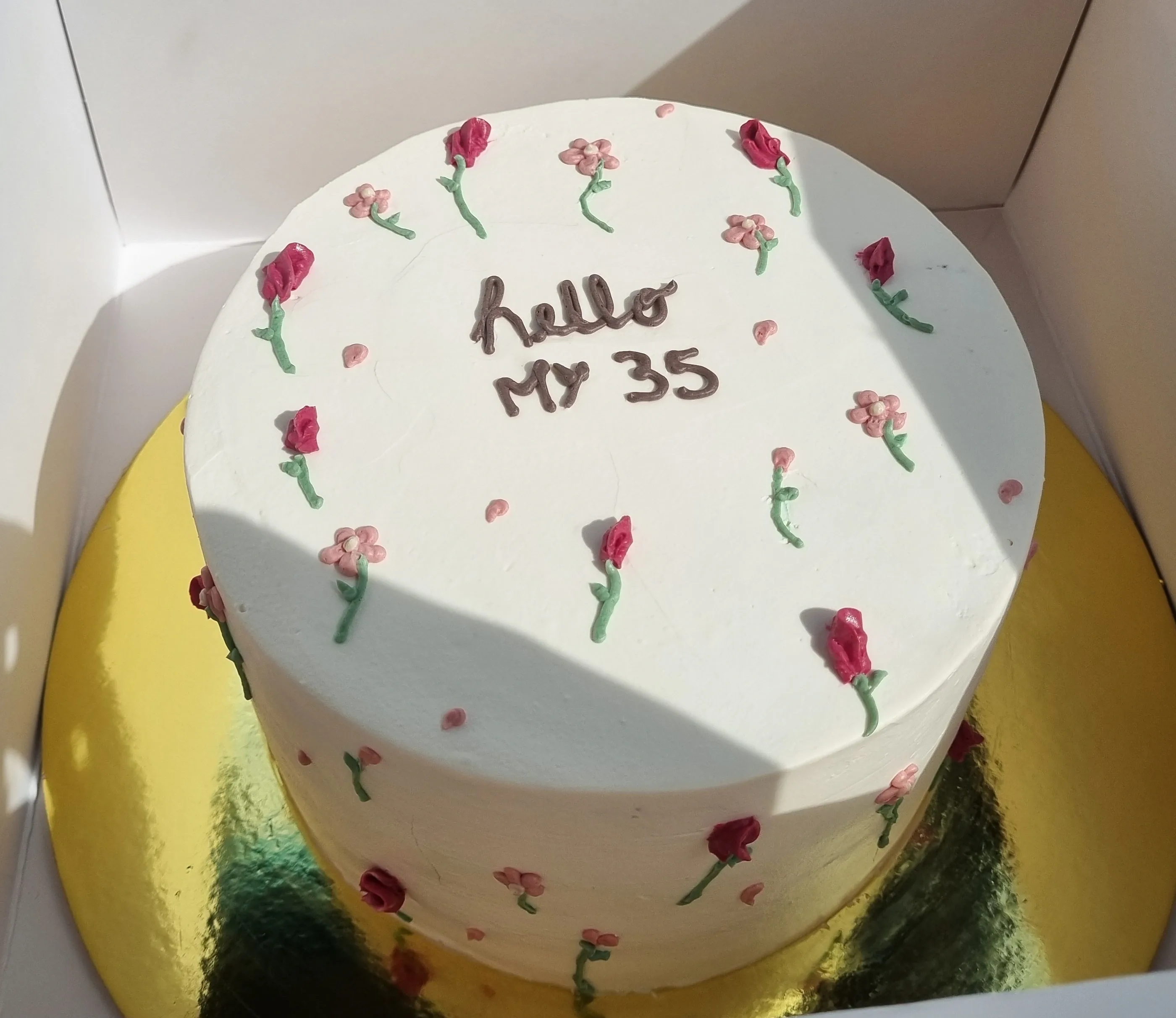 Torta blanca vista desde arriba, decorada con rosas rojas pequeñas e inscripción Hello my 35.