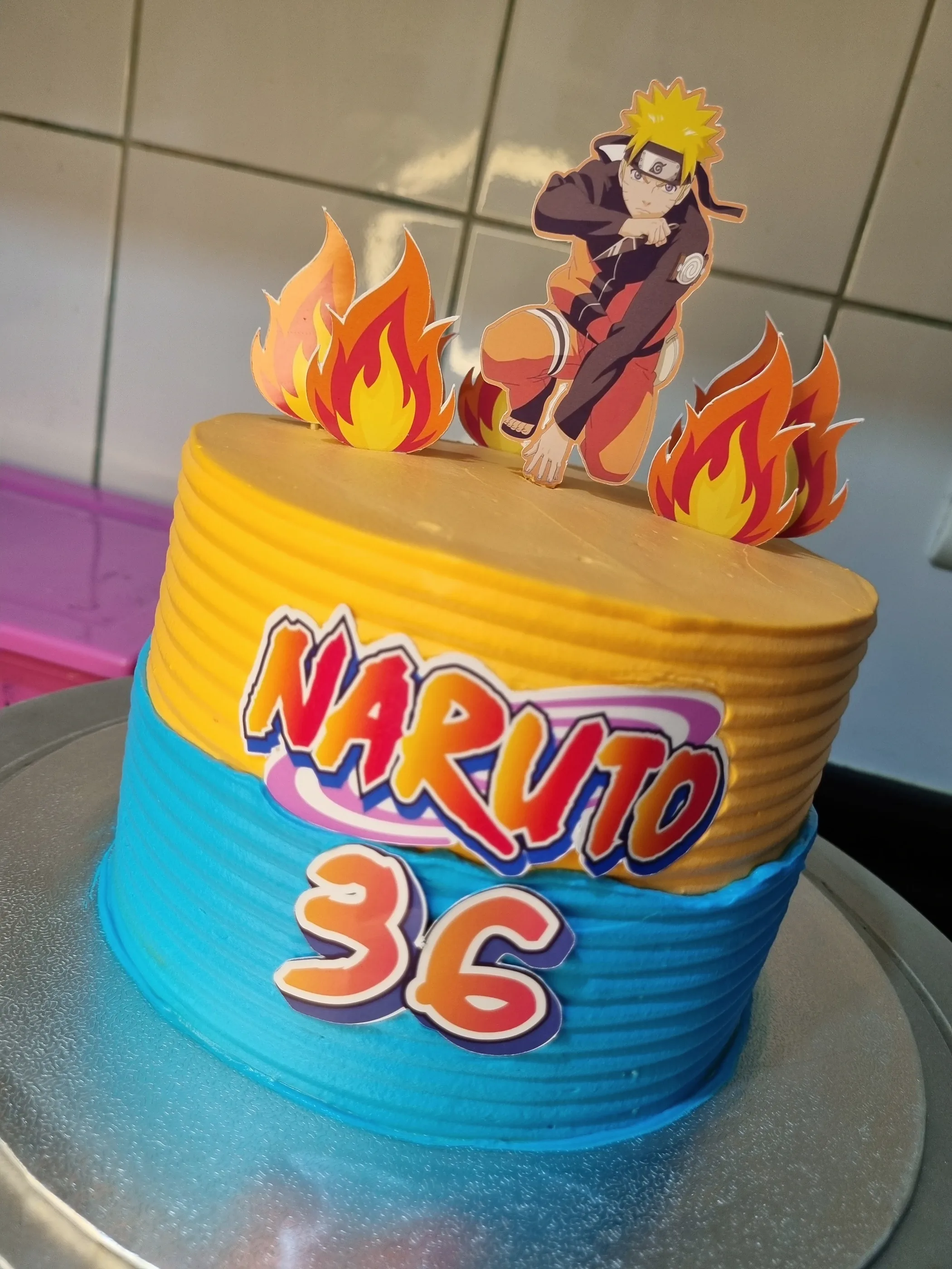 Torta amarilla y azul con decoraciones de Naruto, llamas y número 36.