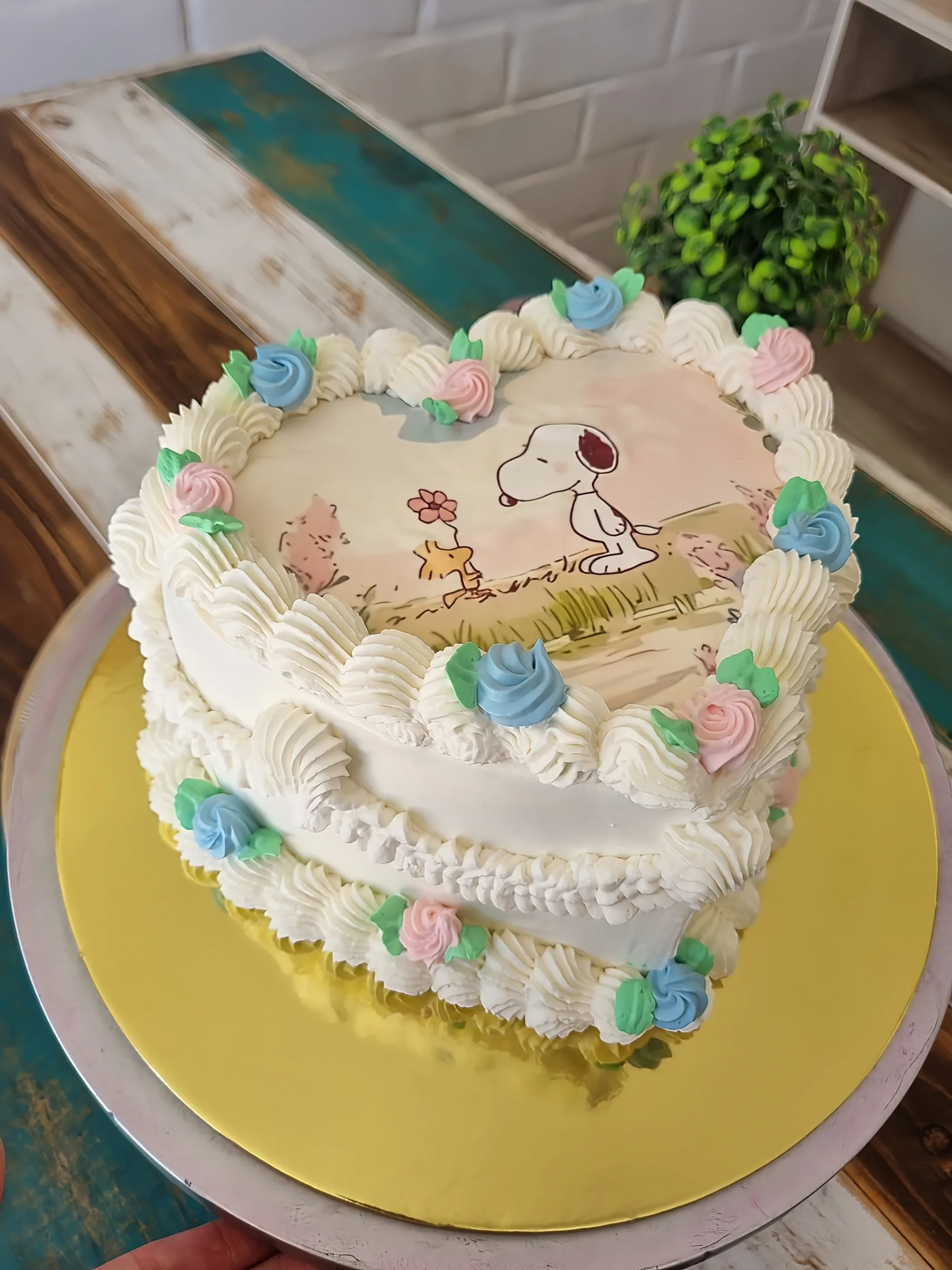 Torta blanca con ilustración de Snoopy y Woodstock, volantes de crema y flores rosadas, verdes y celestes.
