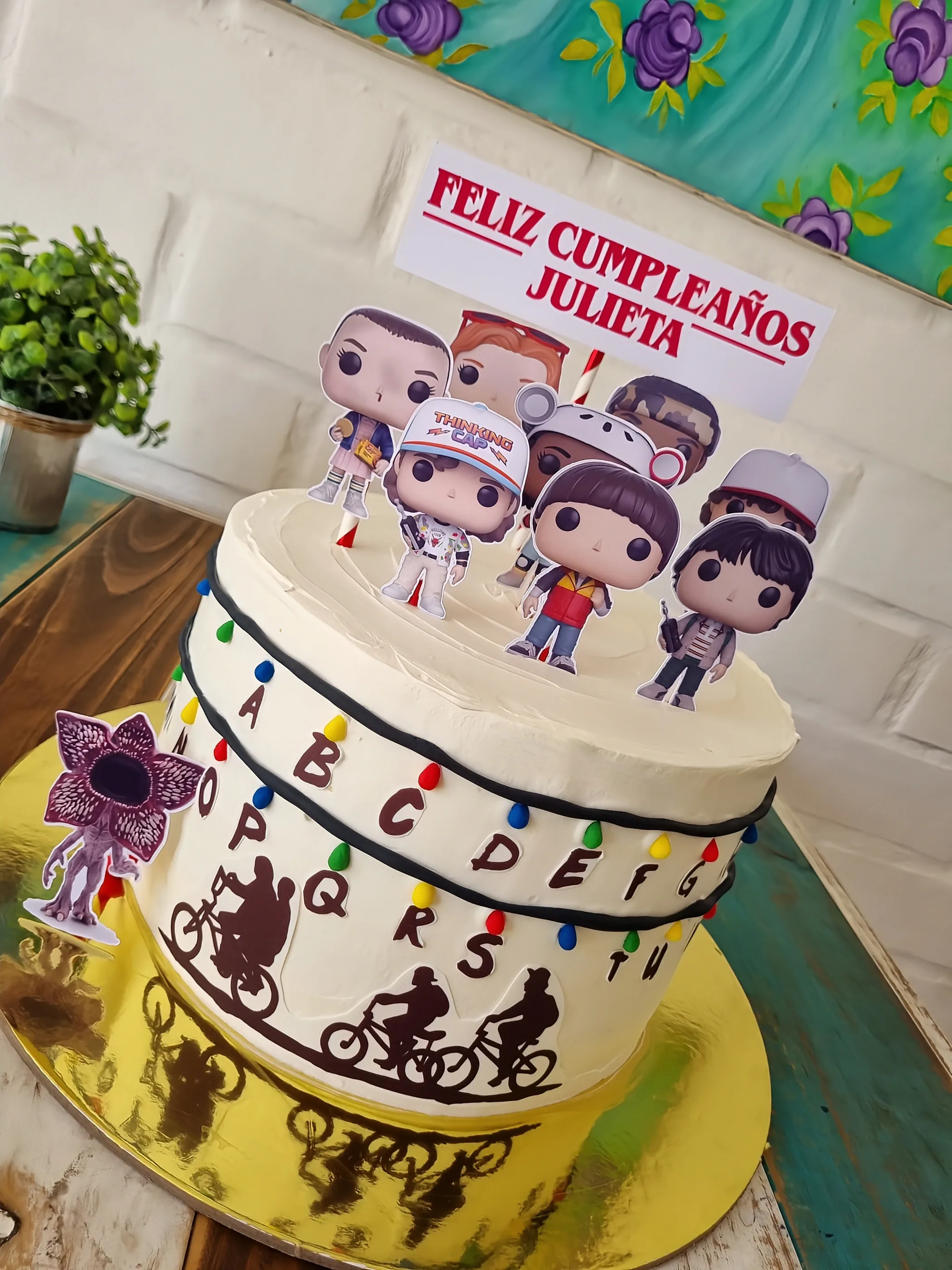 Torta temática Stranger Things con personajes, letras de colores, bicicletas y letrero de cumpleaños para Julieta.