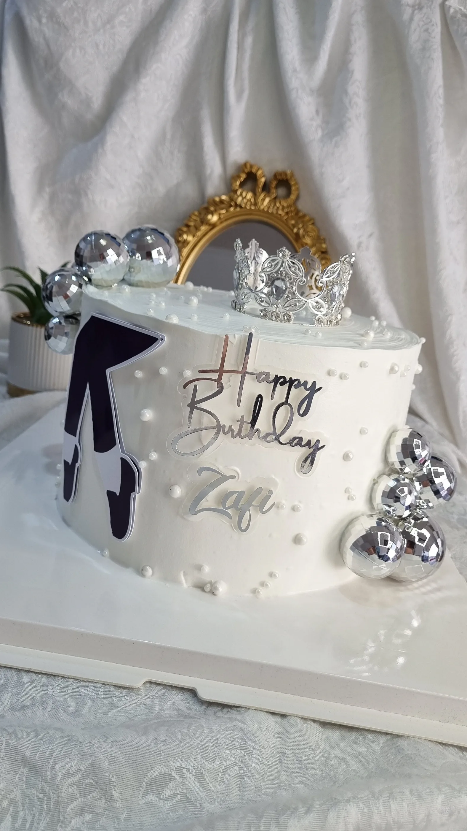 Torta blanca con corona plateada, esferas metálicas, perlas y lazo negro.