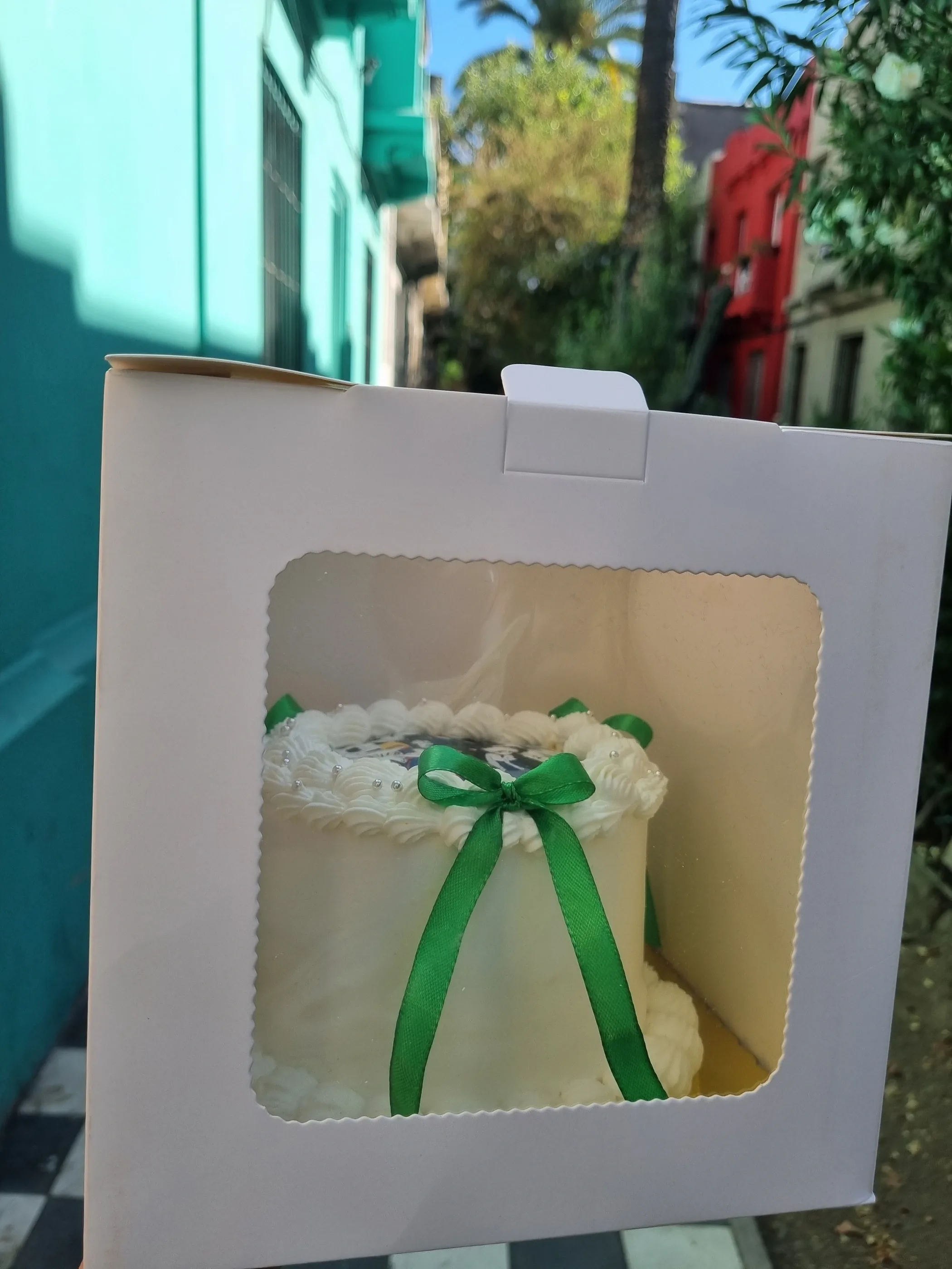 Torta blanca con lazo verde presentada en caja blanca con ventana transparente.