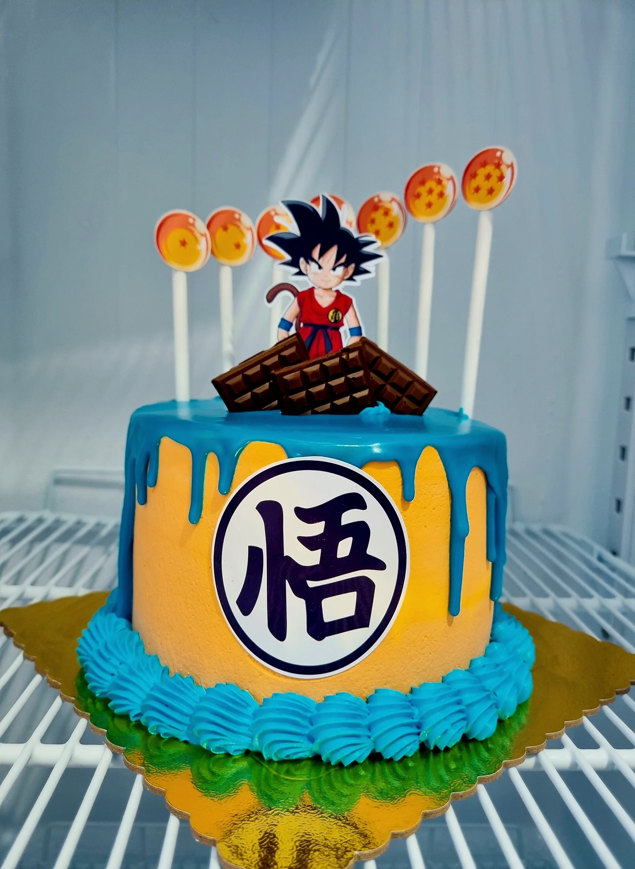 Torta amarilla con goteado azul, personaje Goku, esferas del dragón y símbolo frontal.